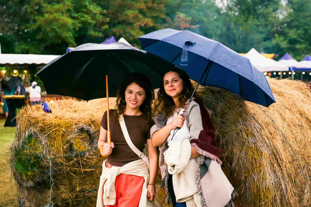two harvest festival-goers with umbrellas in front of hay bales